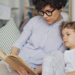 a woman sitting on a couch reading a book to a child
