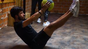 Focused man performing core exercises with a medicine ball in an indoor gym highlighting fitness and strength.